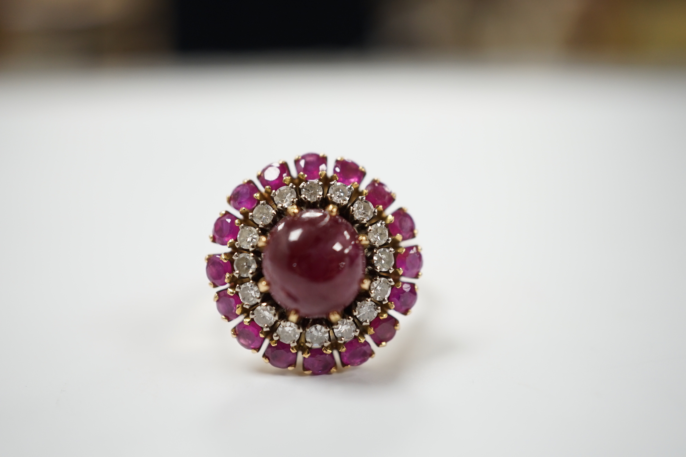 A yellow metal, ruby and diamond set circular cluster dress ring, with central cabochon ruby, size M/N, gross 8.2 grams.